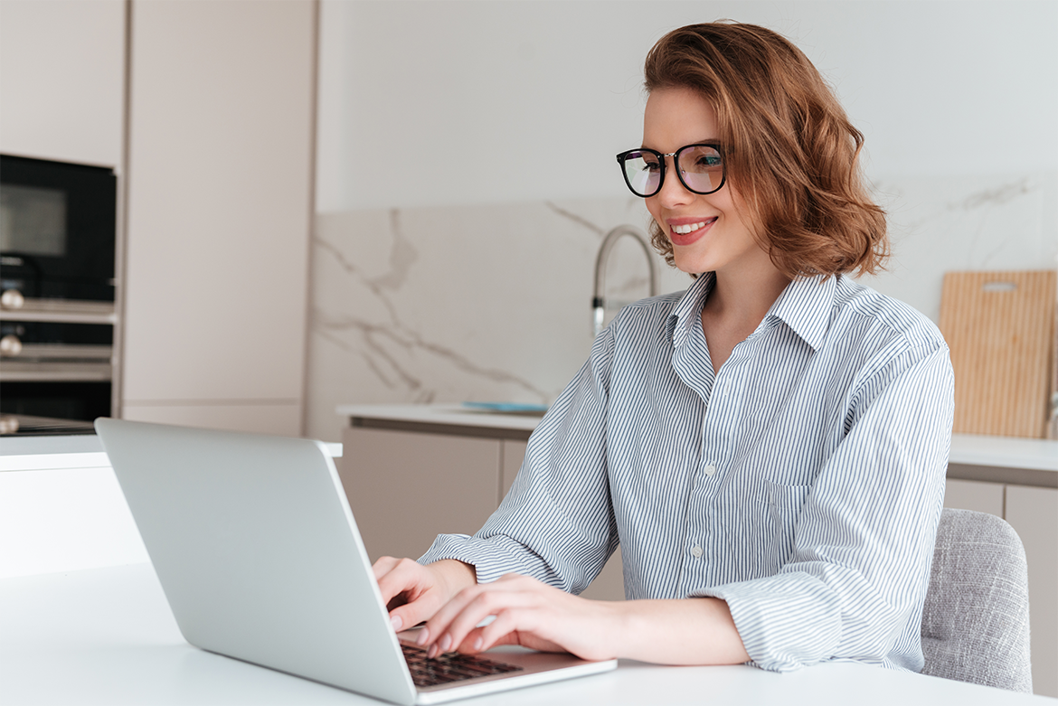 elegant-smiling-woman-glasses-striped-shirt-using-laptop-computer-while-siting-table-kitchen 1170x